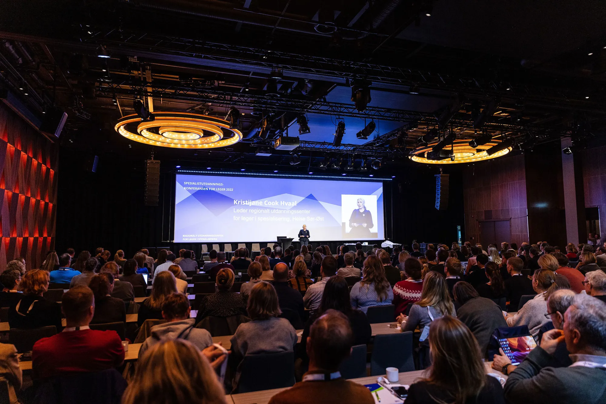 En fullsatt sal sett bakfra med en person stående på scenen