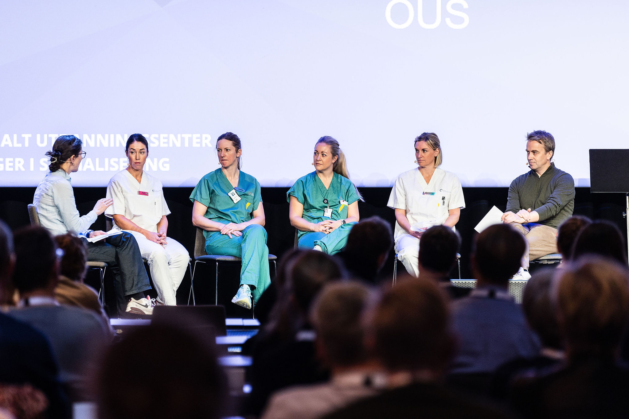 Seks personer som sitter på stoler på scnenen og snakker sammen